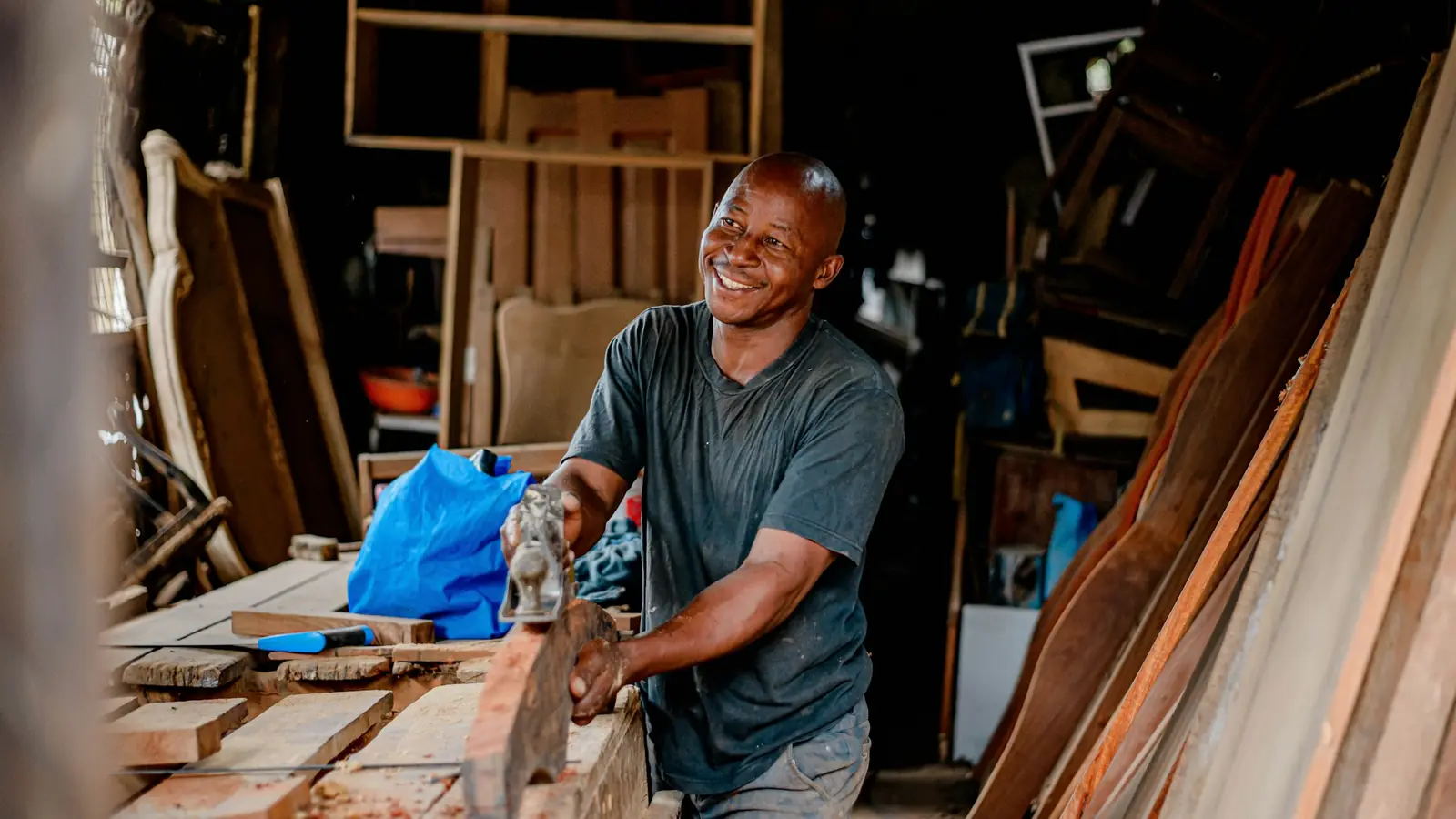 Ein Schreiner lächelt bei der Arbeit an einem Holzbrett in seiner Werkstatt